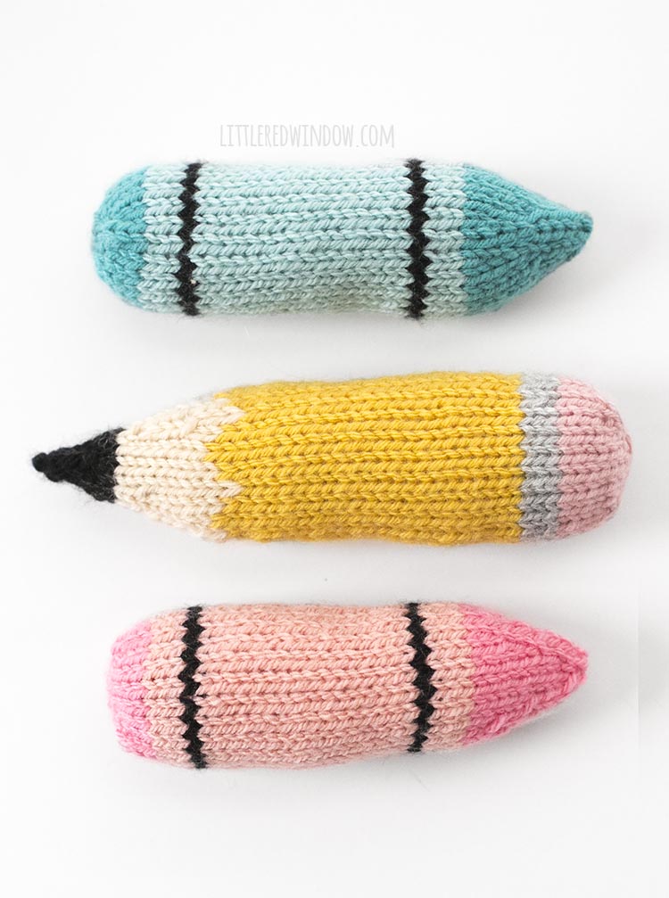 knit blue crayon pencil and pink crayon lined up horizontally on a white background