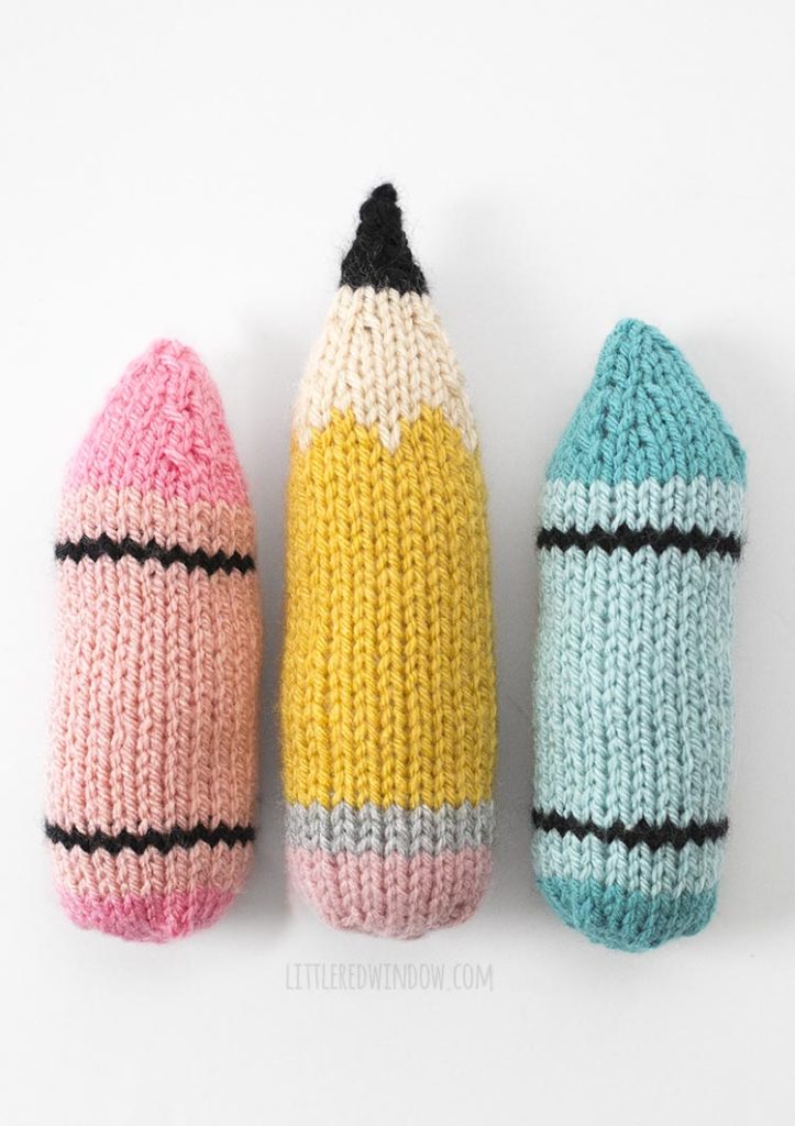 knit pink crayon pencil and blue crayon lined up vertically on white background