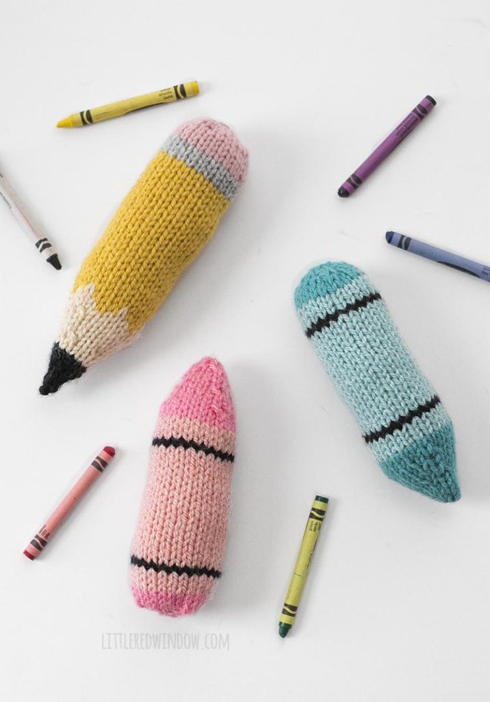 Soft knit pencil and blue and pink background with scattered real crayons
