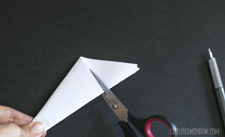 scissors cutting excess paper off the wide end of the folded triangle