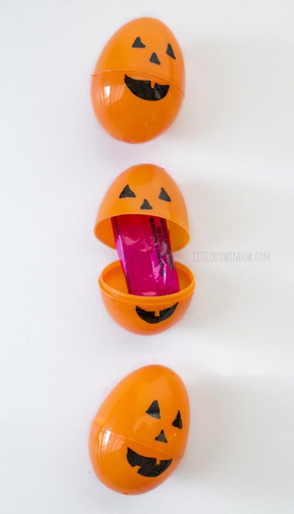 3 orange easter eggs with jack o lantern faces on them one open with candy inside lined up in a vertical row