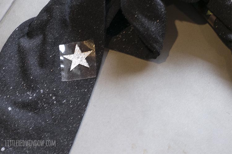 Closeup of silver star iron-on with clear plastic protective film positioned on a black long sleeved tshirt for an outer space costume
