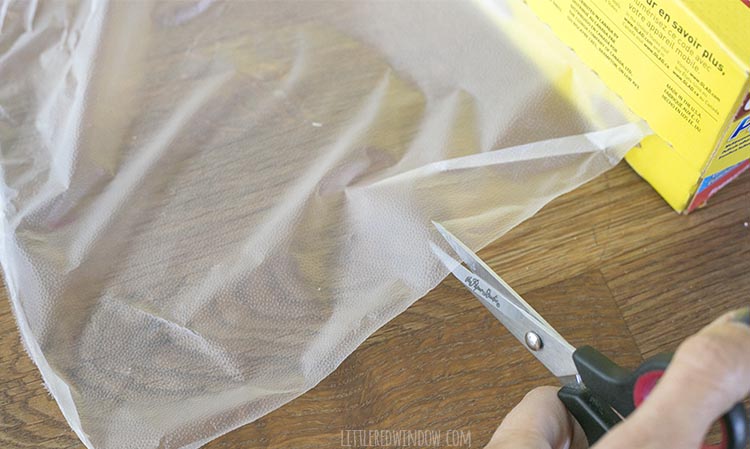 closeup of a pair of scissors cutting into a piece of plastic wrap