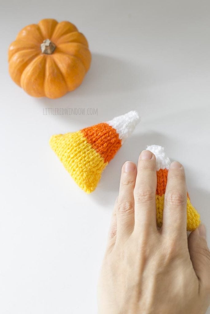 overhead view of hand reaching out over one candy corn handwarmer next to other candy corn shape and mini pumpkin