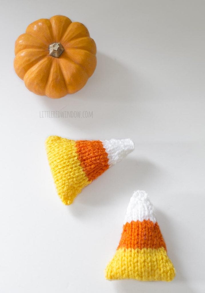 overhead view of two knit candy corn handwarmers and an orange mini pumpkin