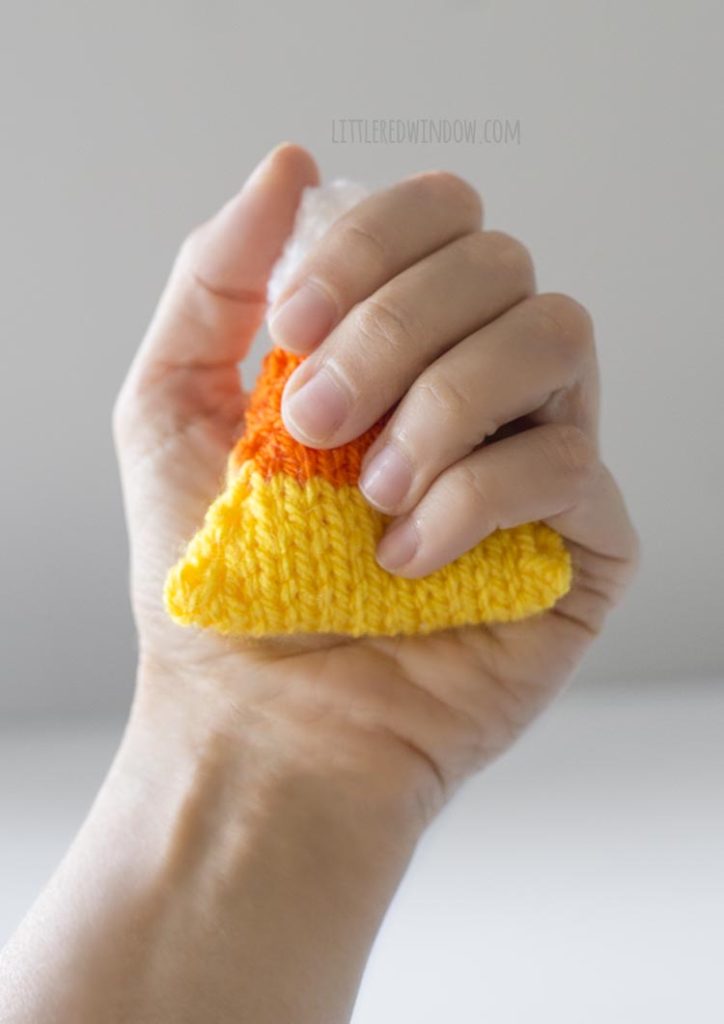 a hand holding one knit candy corn handwarmer