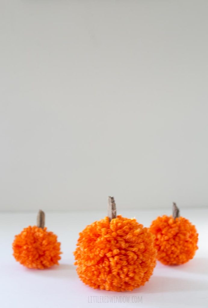 3 orange yarn pom pom pumpkins arranged on a white table