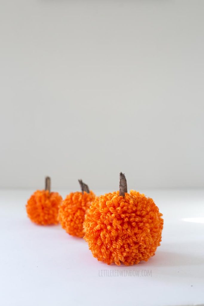 3 orange yarn pom pom pumpkins arranged going back into the distance