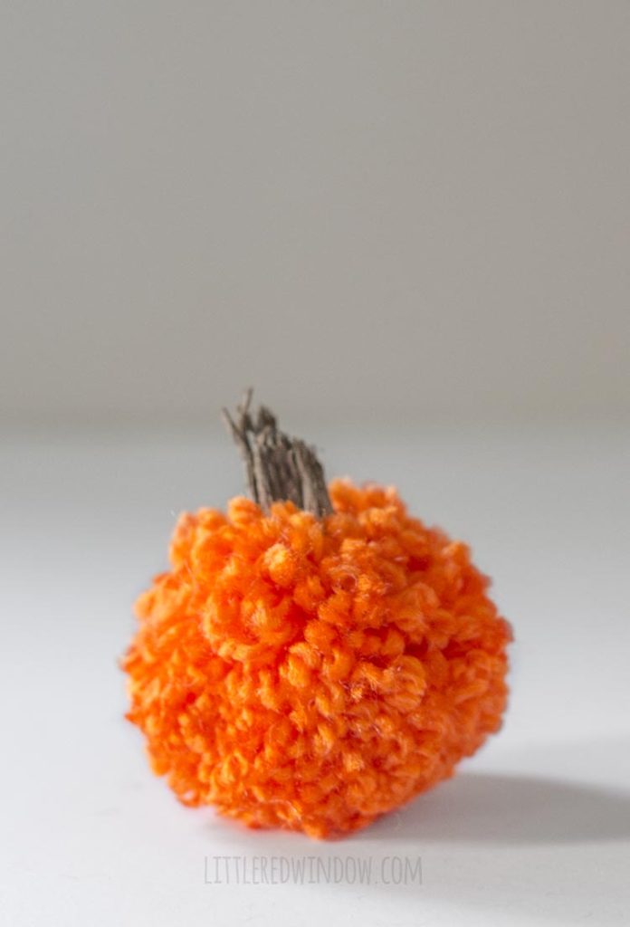 a closeup of a single orange yarn pom pom pumpkin