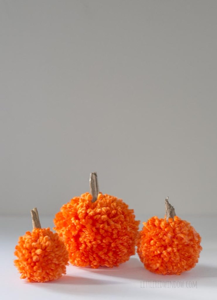 3 orange yarn pom pom pumpkins arranged on a white table