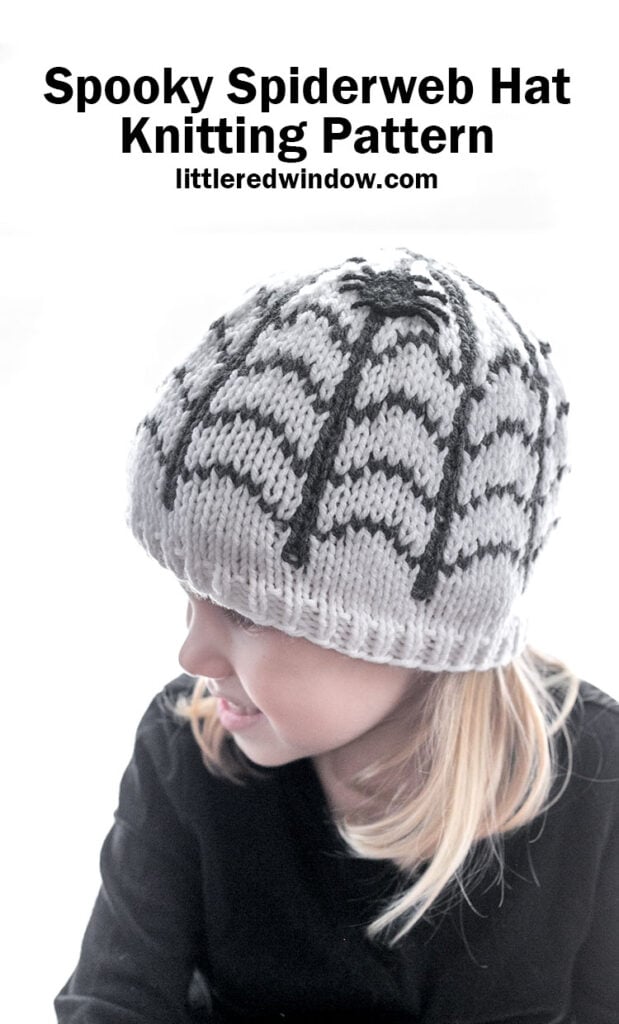 A child wearing a white knitted hat featuring a black spiderweb design and a spider on top, with the title “Spooky Spiderweb Hat Knitting Pattern” above.