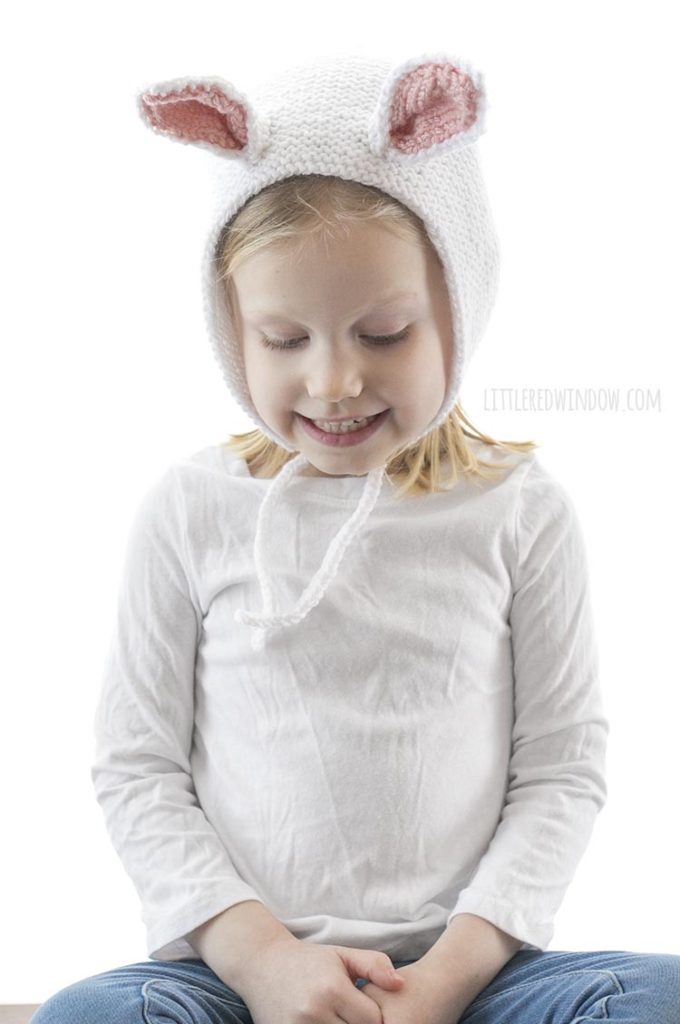 little girl wearing white knit bonnet with bunny ears and looking down