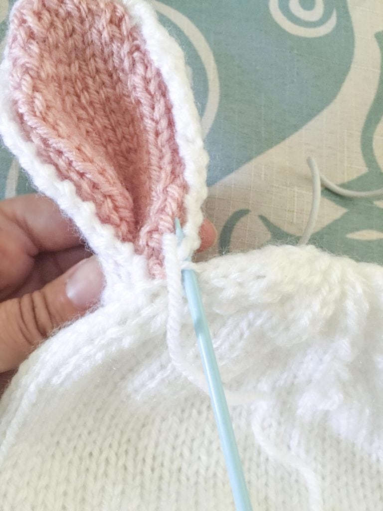 Hand holding a knit bunny ear to sew it on top of a bunny bonnet