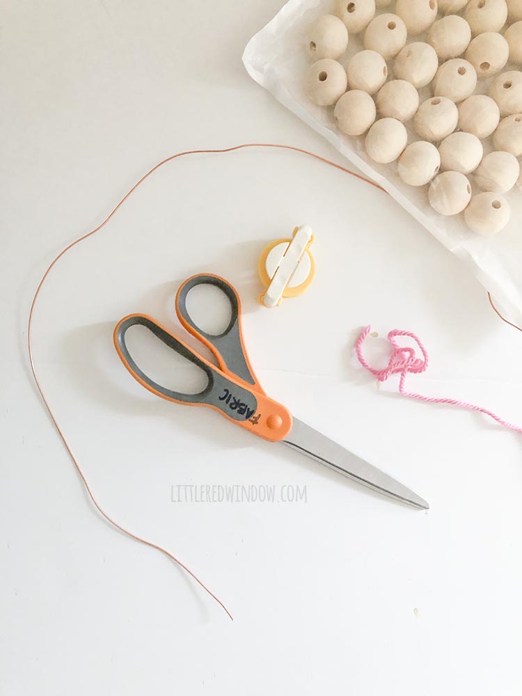 scissors wire pom pom maker and plain round wood beads on a white background