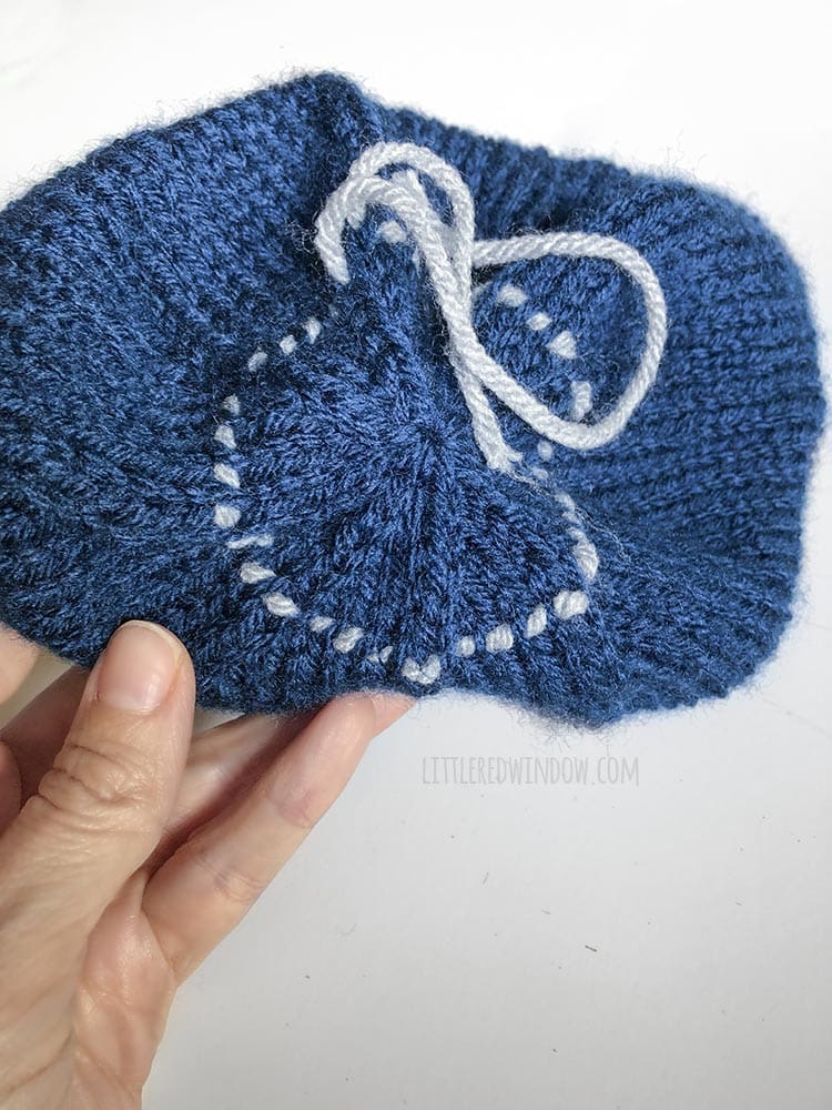 hand holding a blue knit hat with a life line holding a round of stitches around the crown