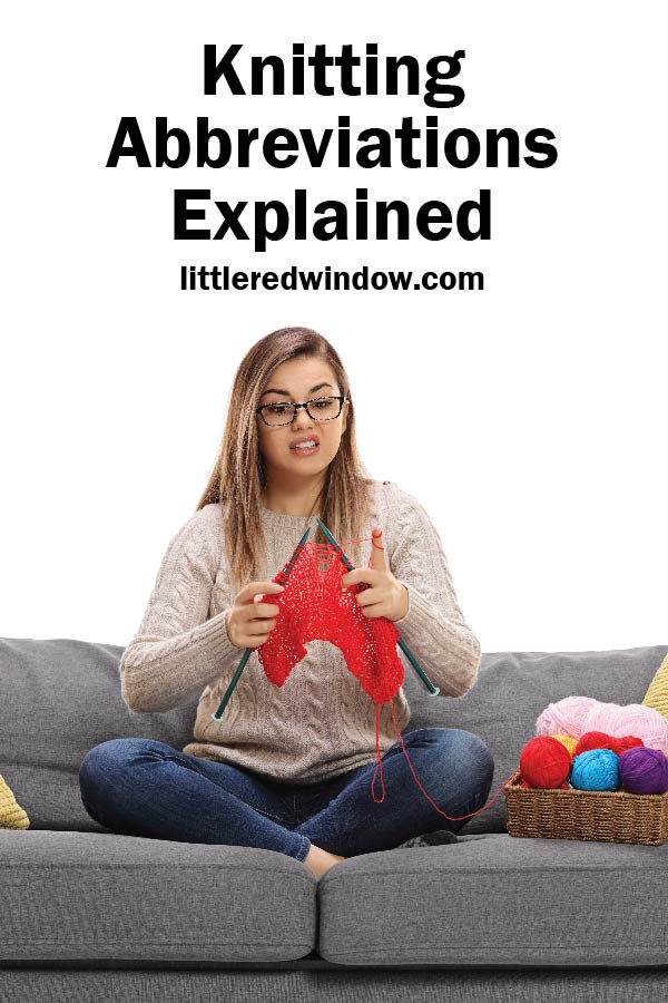 Confused woman sitting on a gray couch looking at her red knitting project