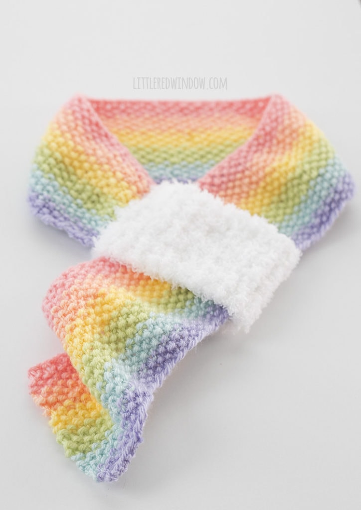 view of pastel rainbow striped knit scarf with white fluffy on a white table
