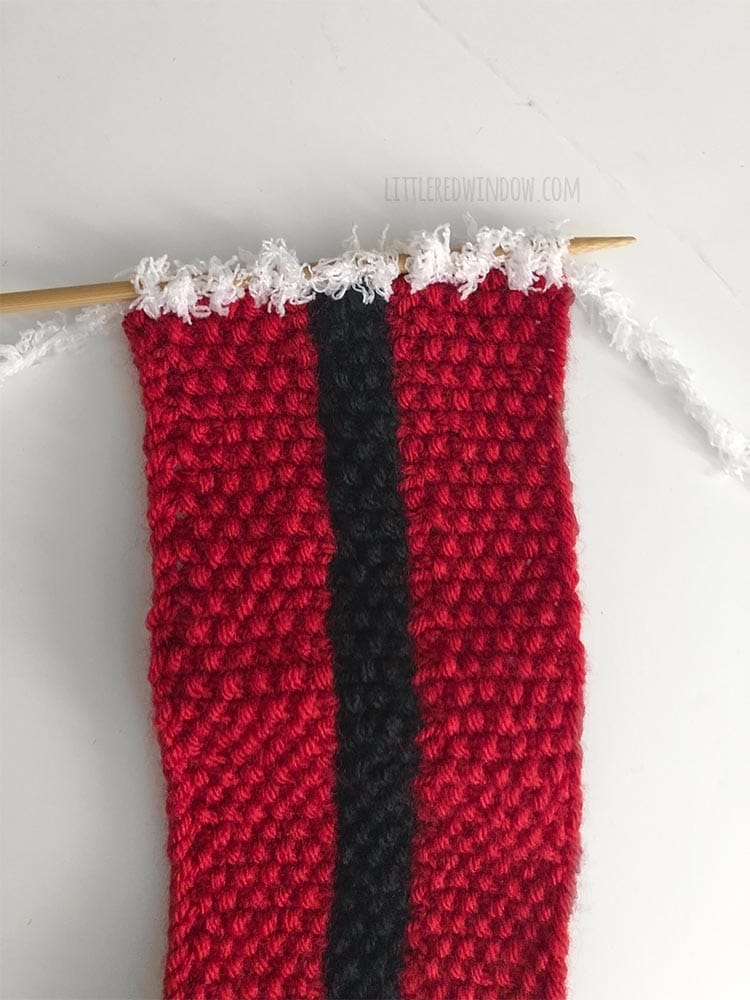 red and black knit scarf with 12 white stitches picked up across one short end