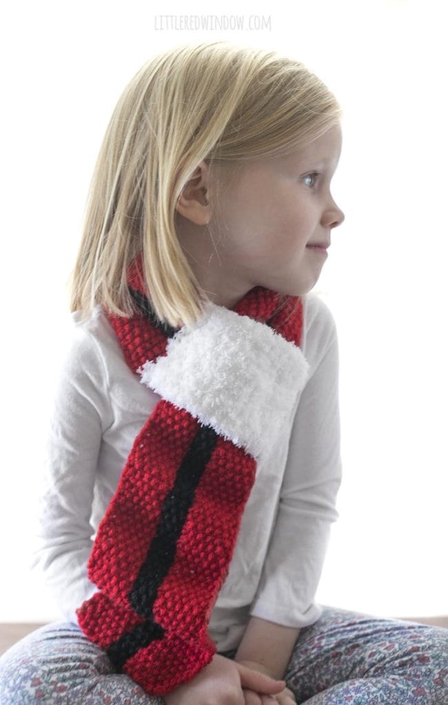 smiling girl wearing red christmas scarf with black stripe and white fluffy end and looking off to the right
