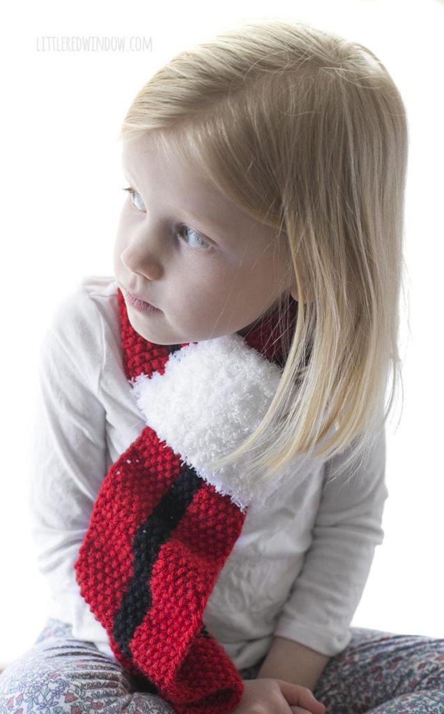 smiling girl wearing red christmas scarf with black stripe and white fluffy end and looking off to the left