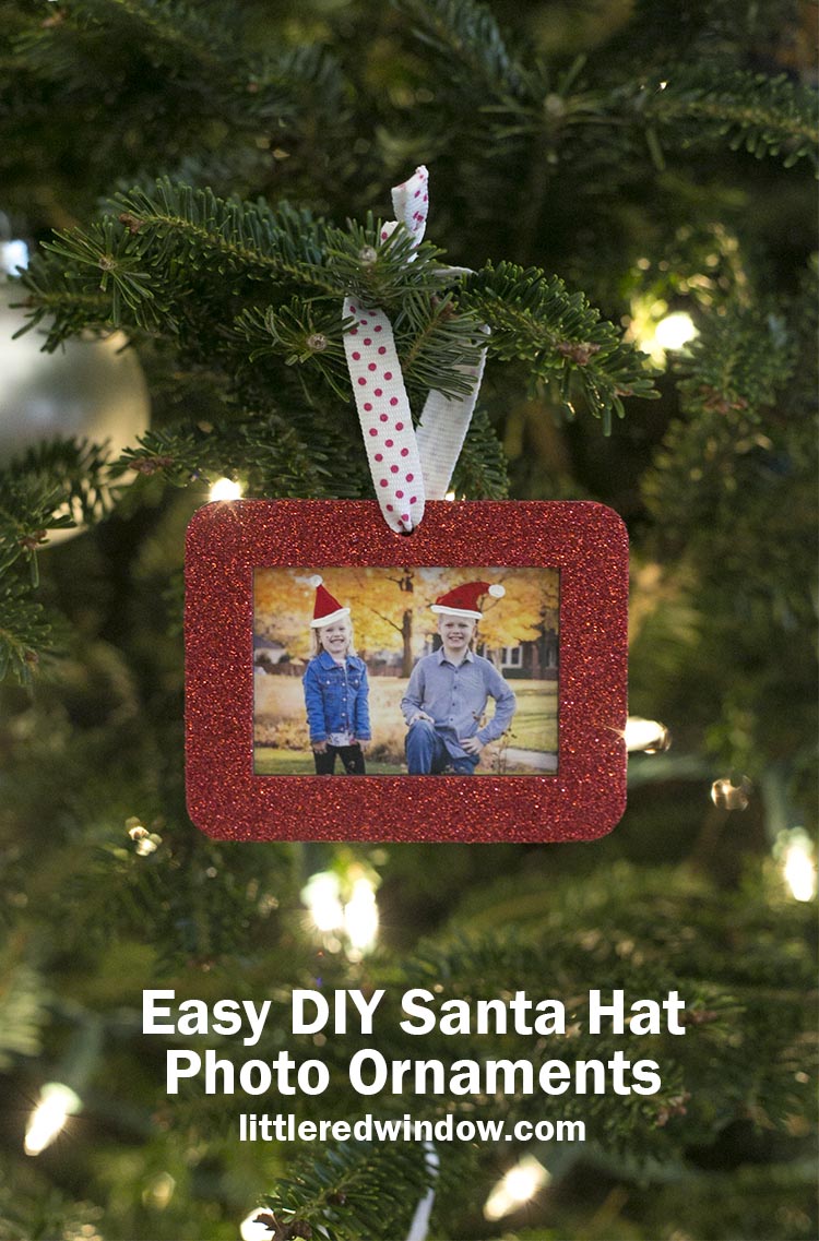 red rectangular glitter photo ornament with a photo of two kids with painted on santa hats inside hanging on a christmas tree with white lights behind