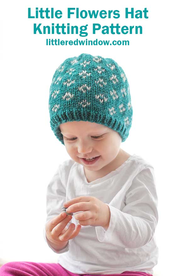 Little girl in teal knit hat with small white flower pattern holding a small seashell