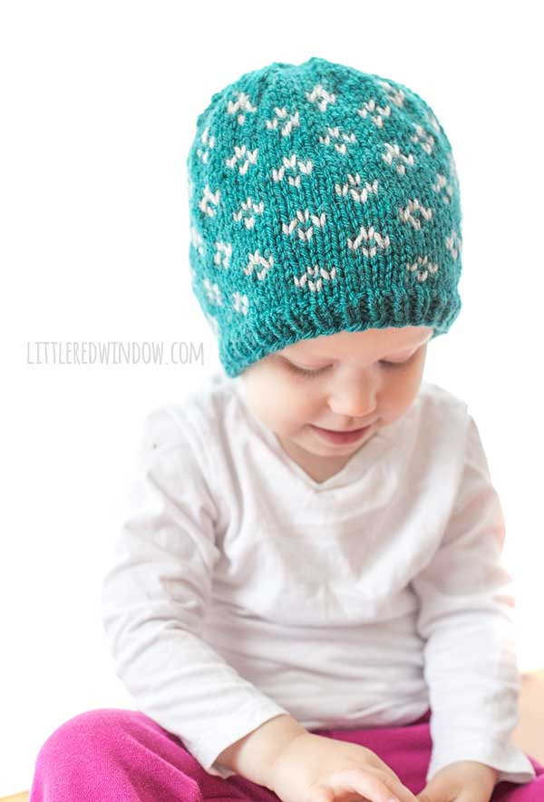 baby in white shirt weraing a teal knit hat with light gray diamonds on it looking down at her lap