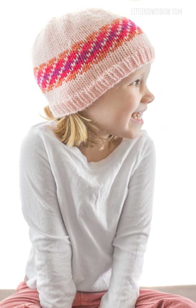 girl in white shirt looking to the right and wearing diagonal stripe fiery fade hat in light pink orange magenta and purple fade