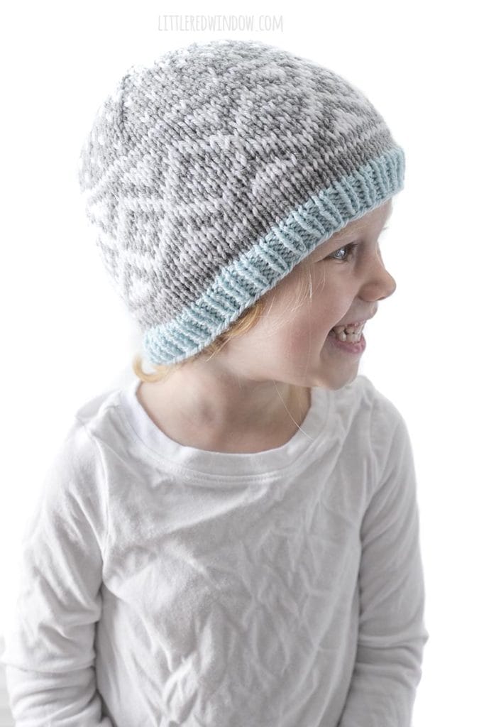smiling girl looking off to the right and wearing gray and white knit diamond snow pattern hat