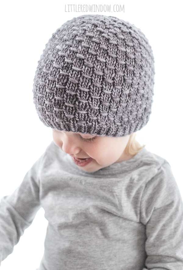 smiling girl in gray shirt looking down at her lap and wearing gray knit elm grain stitch knit hat