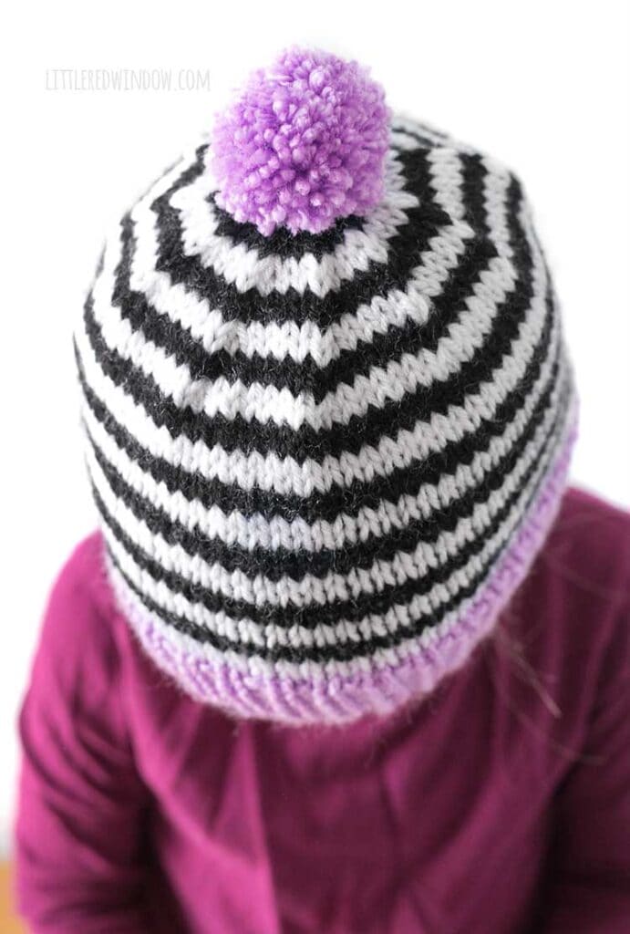 top view of black and white striped Fun stripe hat with purple pom pom on top