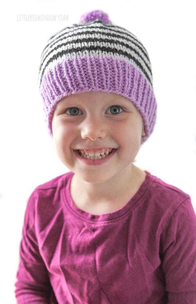 little girl in black and white striped fun stripe hat smiling at the camera