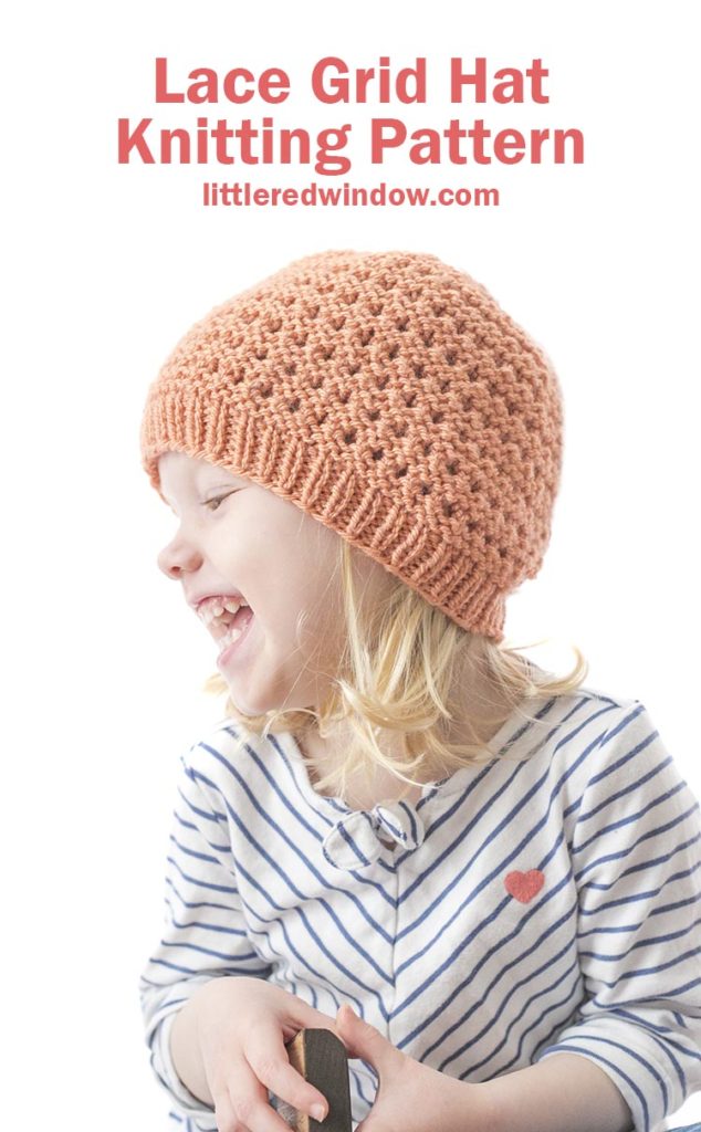 laughing girl in white shirt with navy stripes and a coral colored knit lace grid hat looking off to the left 