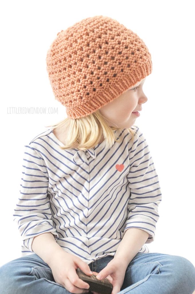 little girl in coral knit lace grid hat looking back over her left shoulder