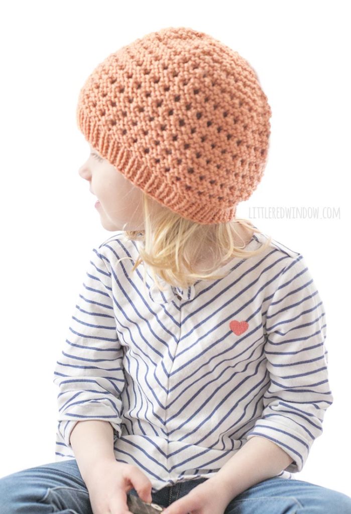 little girl in coral knit lace grid hat looking back over her right shoulder