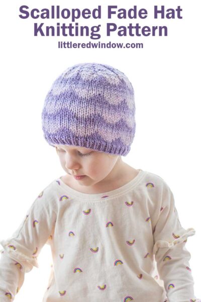 little girl wearing purple knit hat with ombre scallops pattern looking down and to the left at her hand