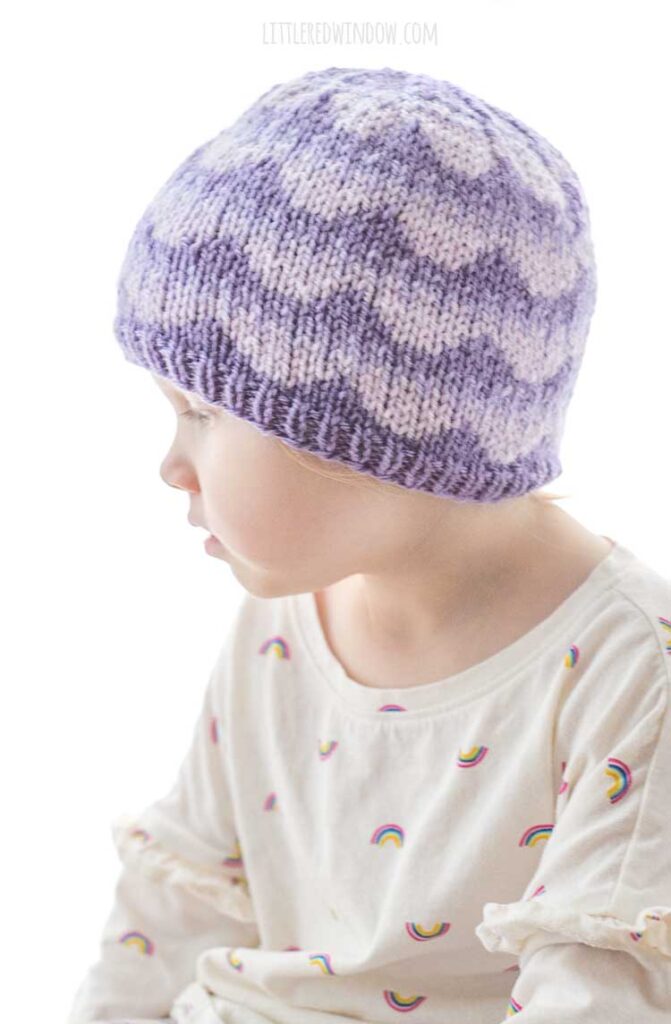 little girl wearing purple knit hat with ombre scallops pattern looking off to the left