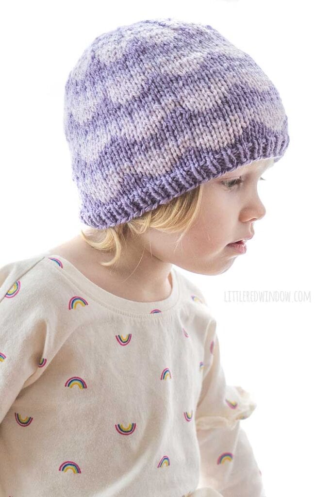 little girl wearing purple knit hat with ombre scallops pattern looking off to the right