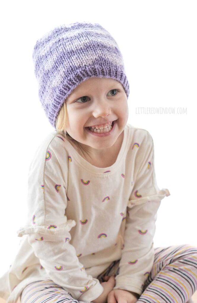 little girl wearing purple knit hat with ombre scallops pattern and smiling at the camera