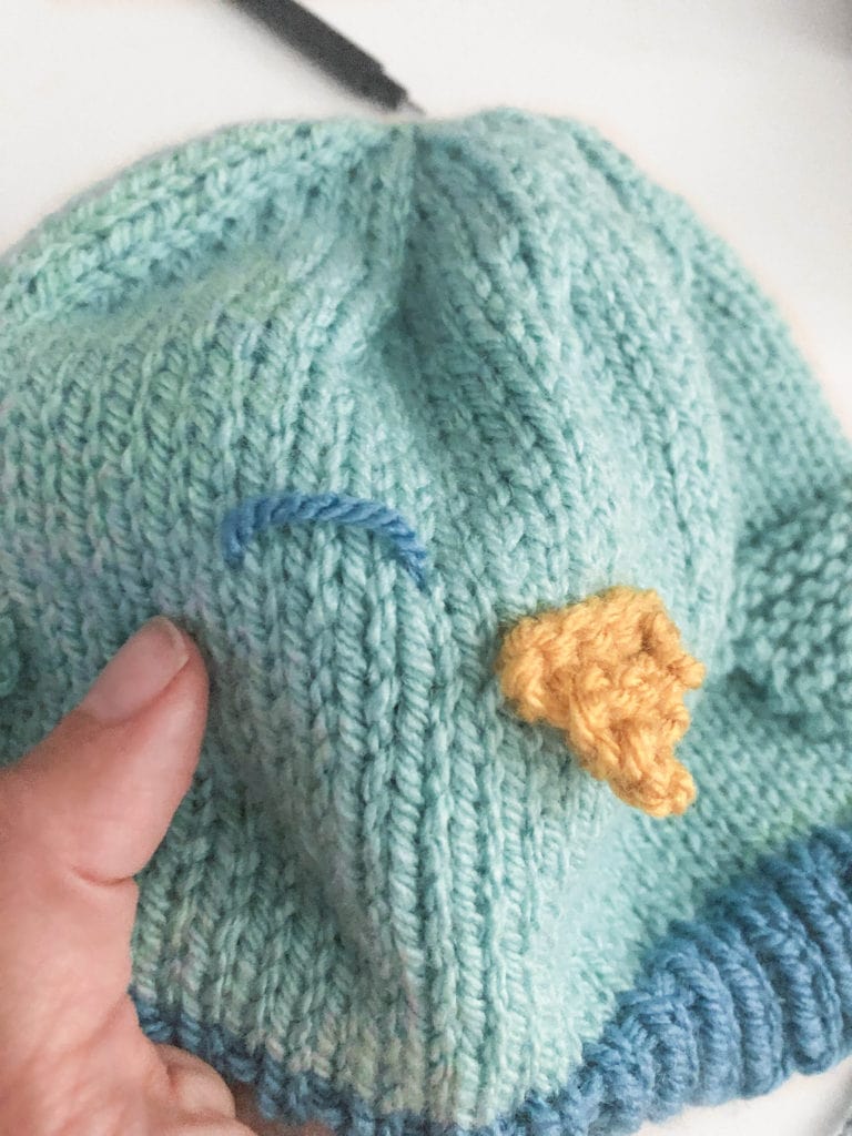 hand showing hat with upside down u shaped stitch for the bluebird eyes