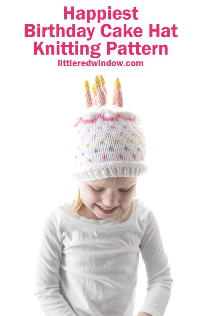 little girl in white shirt smiling looking down and wearing a knit hat that looks like a birthday cake with candles on top 