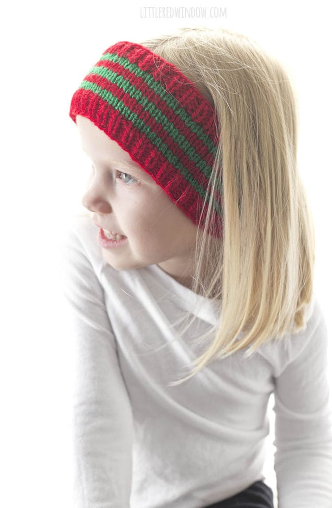 little girl in white shirt wearing red and green striped knit headband and looking off to the left