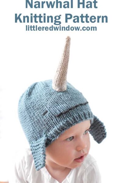 child in white shirt wearing a medium blue knit hat that looks like a narwhal in front of a white background looking off to the right