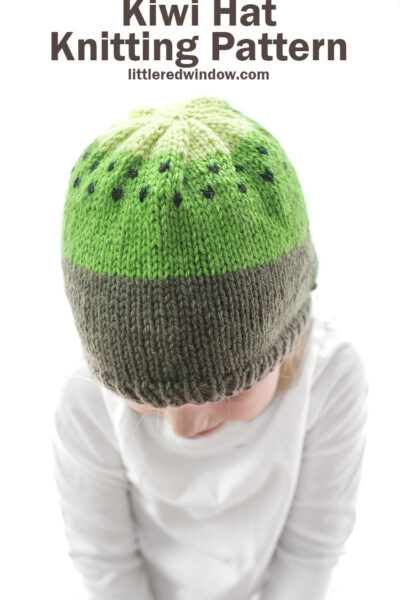 small child modeling brown and green knit kiwi hat knitting pattern with black seeds