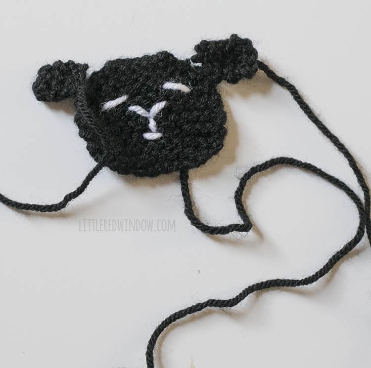 black round knit sheep face with little knit ears sitting next to it to show where to sew them on