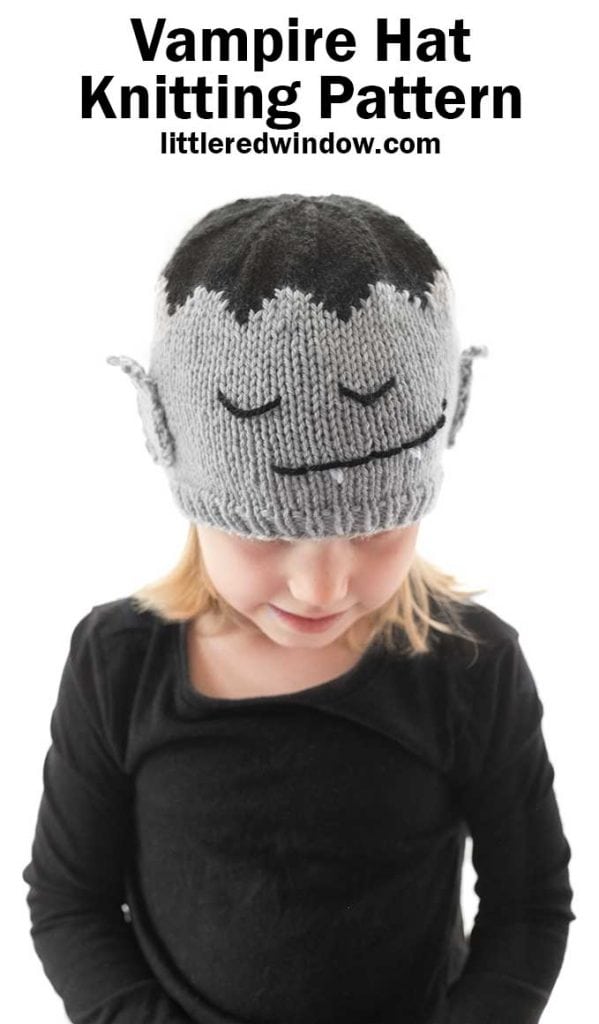 little girl in black shirt wearing gray and black knit hat with a vampire face on it