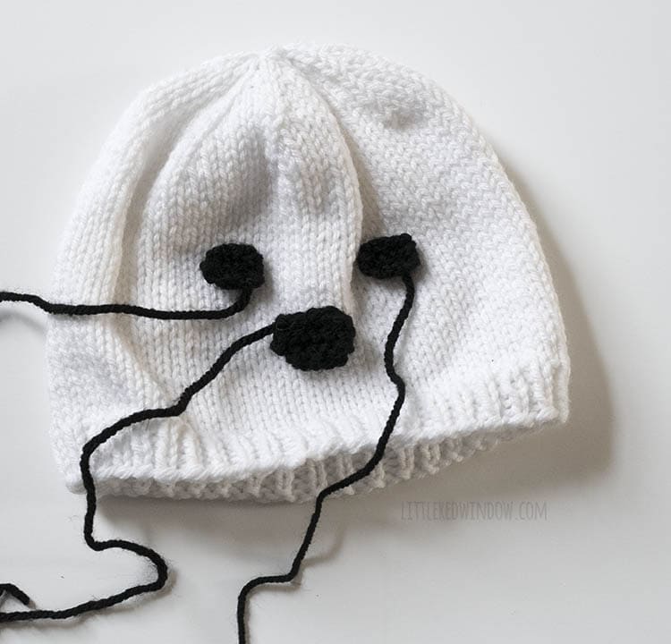 white knit hat with black knit circles laid on top to look like a nose and eyes