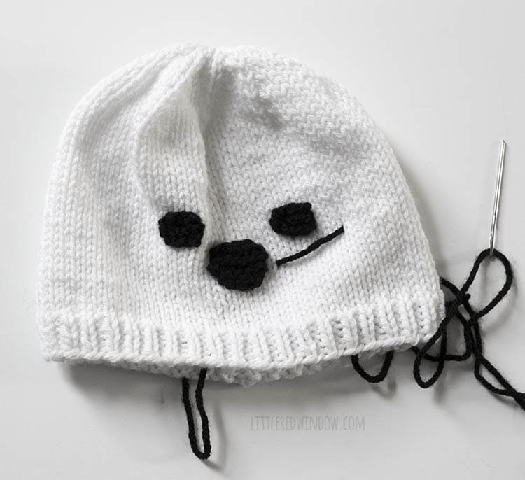 white knit seal hat with one whisker stitched on with black yarn