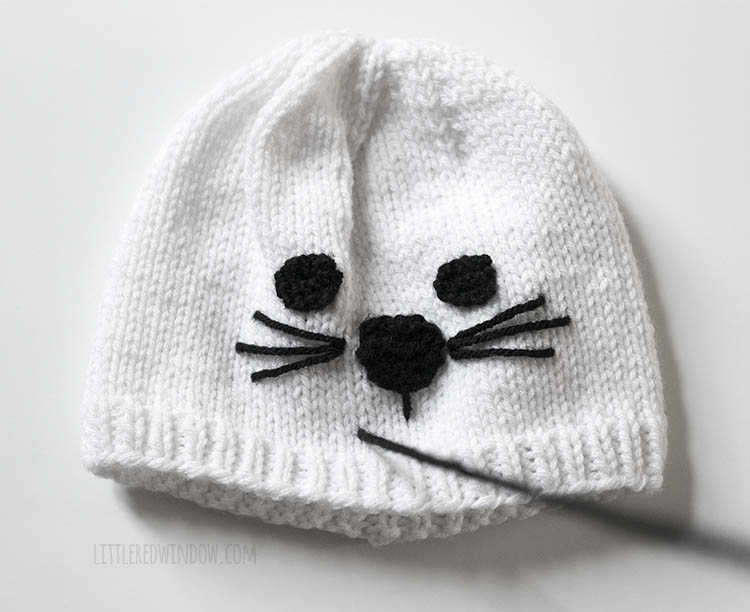 white knit seal hat with a piece of black yarn stitching the mouth