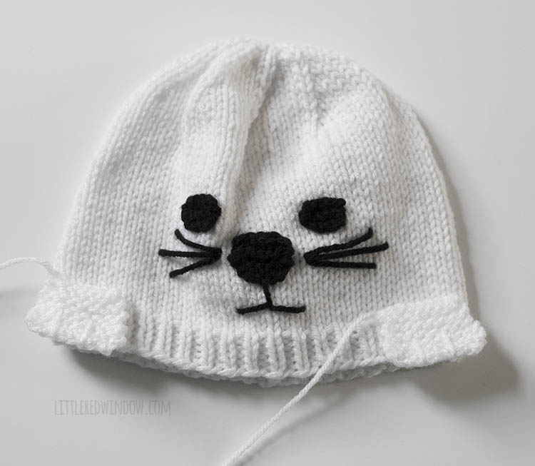 white seal knit hat with paws placed on top to show where to sew them on the front of the hat just above the ribbed brim